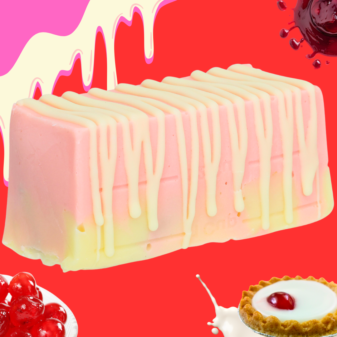 A rectangular handmade Bakewell Tart Fudge bar in pastel pink and yellow with white icing drizzle, set on a vibrant red background surrounded by cream splashes, cherries, and a cherry tart.