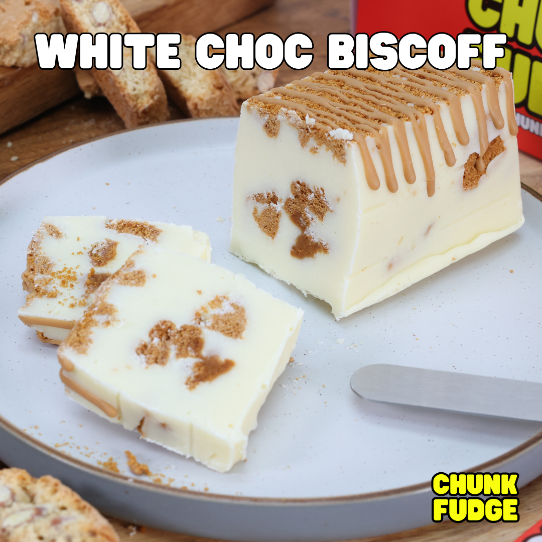 A partially sliced block of White Choc Biscoff Fudge sits on a plate with a spreading knife. Crushed Lotus Biscoff biscuits top the creamy fudge, adding caramel crunch. The text reads WHITE CHOC BISCOFF and CHUNK FUDGE.