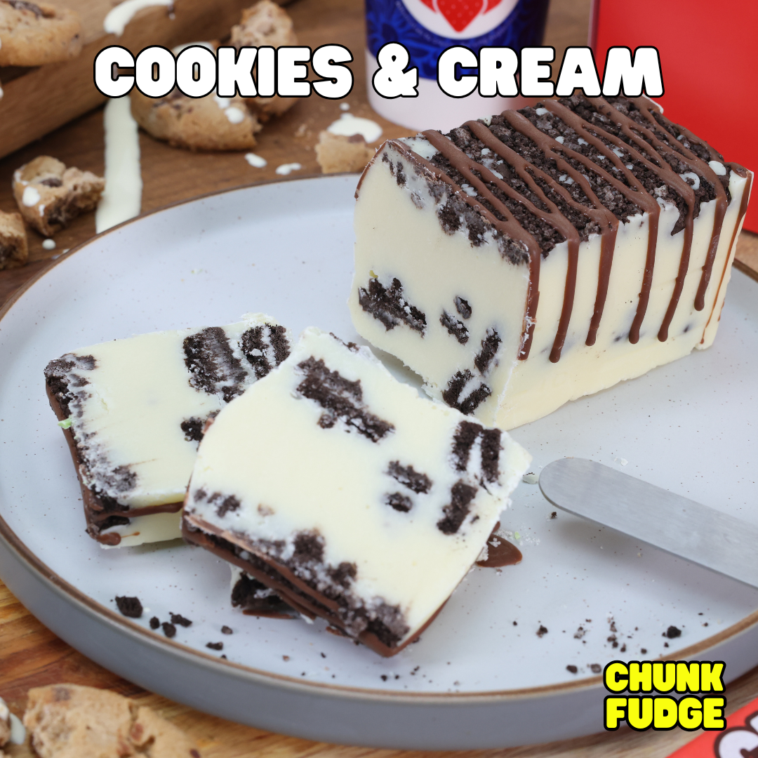 Thick slices of handmade Cookies And Cream Fudge—white fudge with cookie pieces and a chocolate drizzle—are on a plate. "Cookies And Cream Fudge" is shown above, with nearby cookie crumbs and a butter knife.
