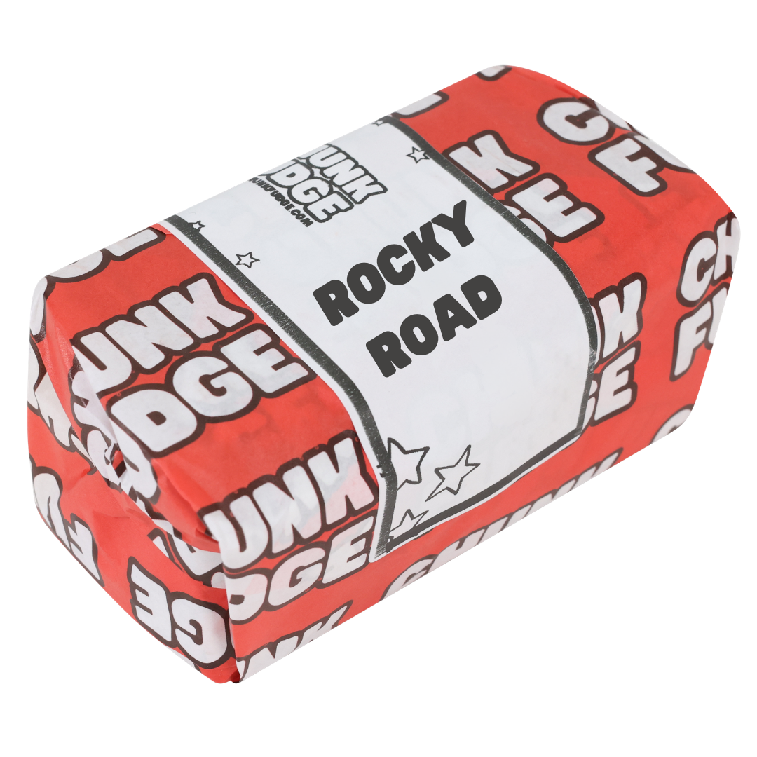 A rectangular block wrapped in red and white paper labeled "Rocky Road Fudge," featuring star designs, resembles classic candy or handmade fudge packaging.
